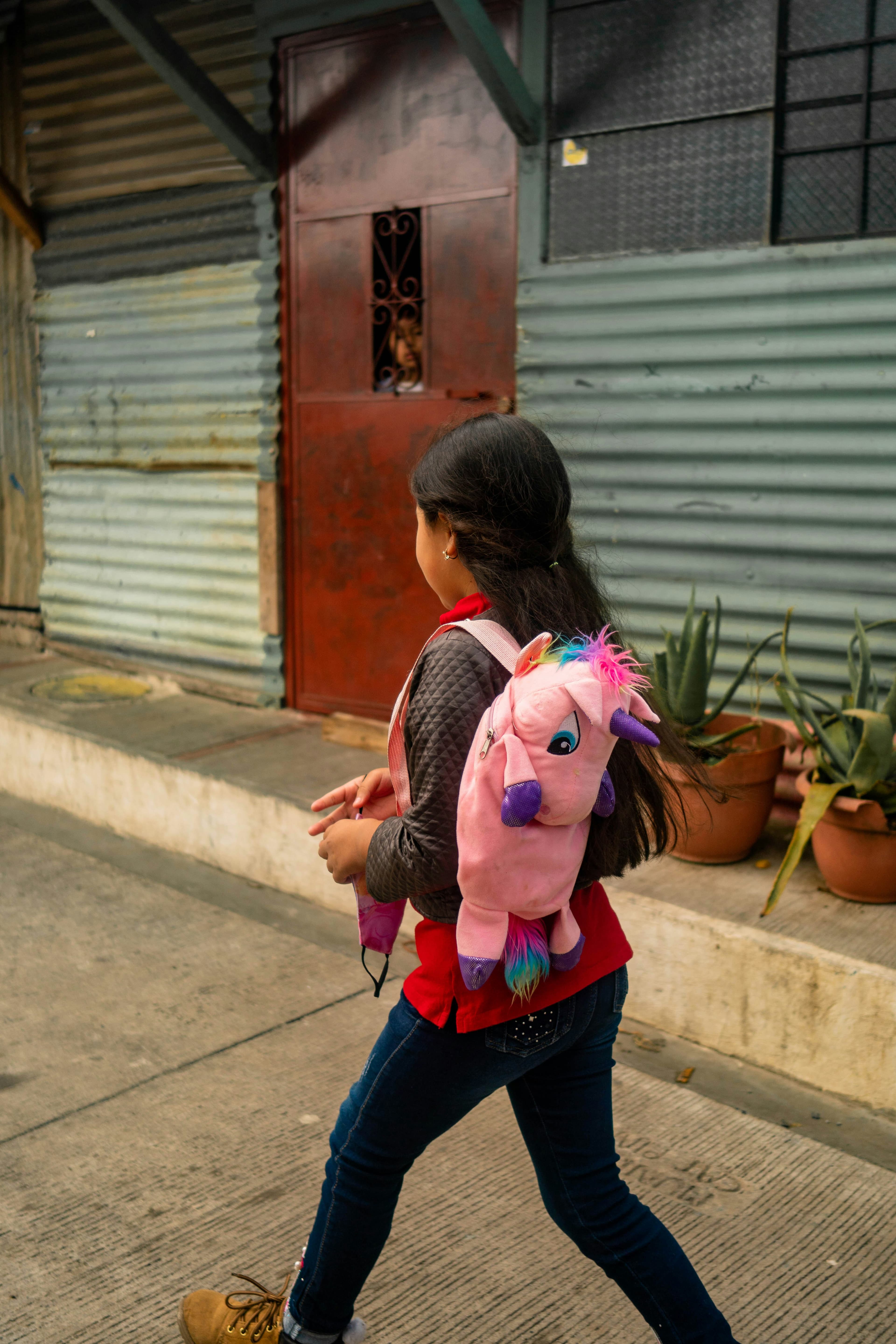 Niña con mochila de peluche en forma de unicornio color rosa camino a la escuela.